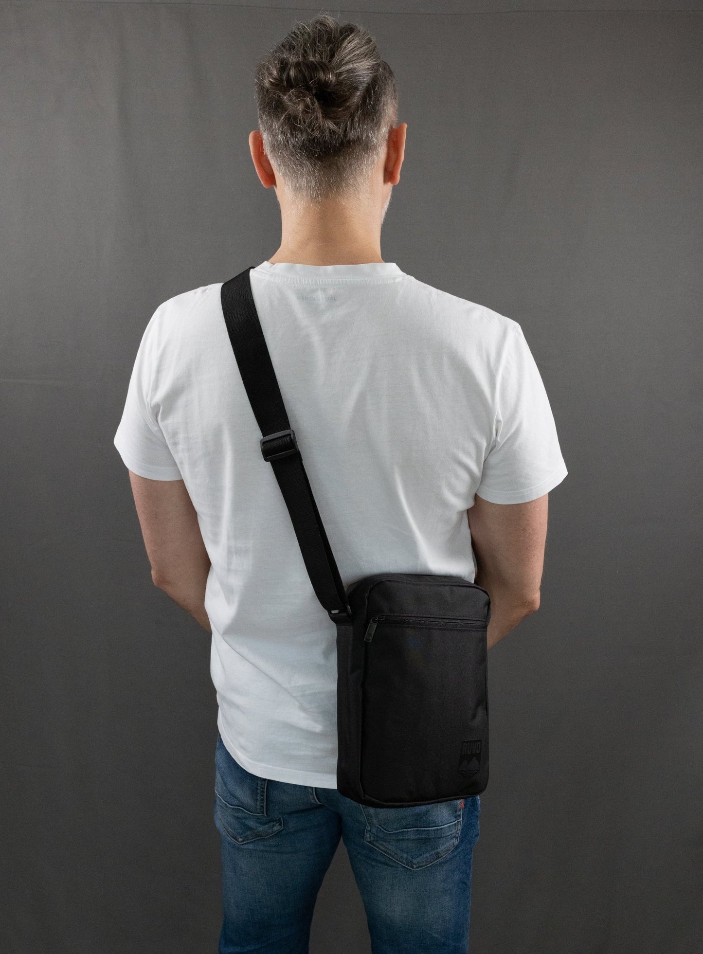 RUVO Umhängetasche Sling Bag mit männlichen Modell. Das Modell trägt ein weißes T-Shirt und eine blaue Jeans. Das Modell trägt die Umhängetasche über die linke Schulter.