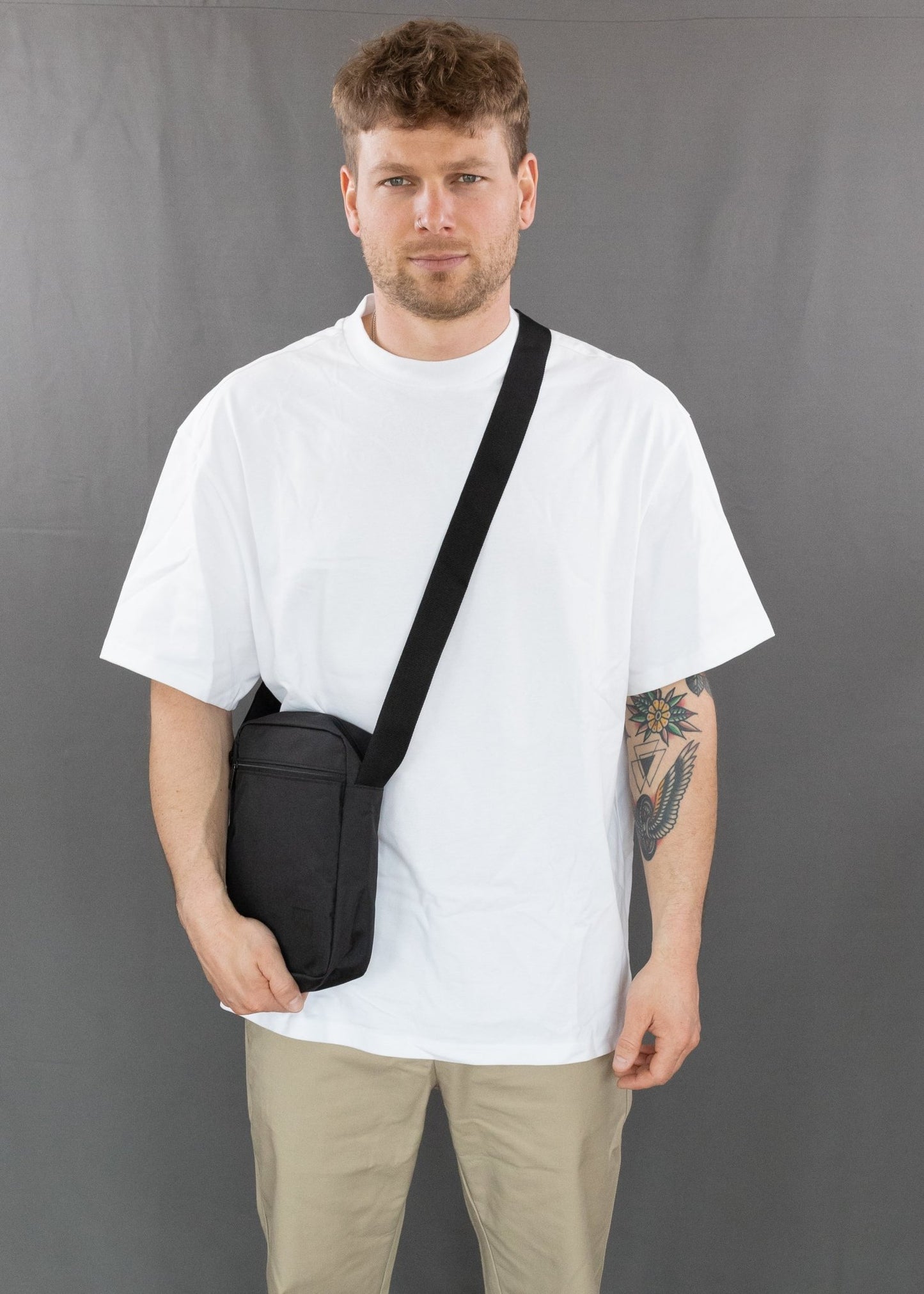 RUVO Umhängetasche Sling Bag Größe M in schwarz. Modell trägt die Tasche über der linken Schulter und man sieht das Modell von vorne. Die Hand des Modells liegt an der Tasche an.