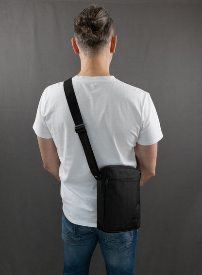RUVO Umhängetasche Sling Bag mit männlichen Modell. Das Modell trägt ein weißes T-Shirt und eine blaue Jeans. Das Modell trägt die Umhängetasche über die linke Schulter.